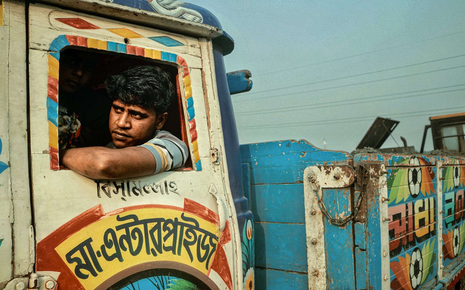 Portrait of a man leaning out of a vibrantly decorated truck in Dhaka, Bangladesh.